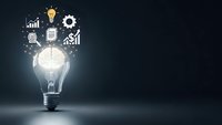 Business innovation concept with glowing lightbulb and floating icons representing growth, strategy, and success on dark background with copy space.