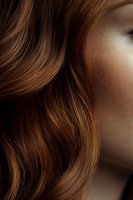 Close-up of wavy brown hair with natural highlights and soft texture against blurred skin background, showcasing healthy, flowing locks for beauty and haircare advertising.