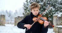 Young Caucasian male musician playing violin outdoors in snowy winter landscape. Classical music performance in cold weather with evergreen trees background.