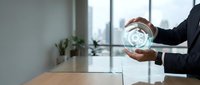 Businessman holding glowing globe hologram at office desk with city skyline view, representing global business, technology innovation, and international corporate strategy.