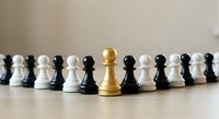Golden pawn standing out among black and white chess pieces on wooden surface, representing leadership, uniqueness and strategic thinking in business.
