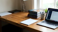 Modern home office workspace with laptop computer and books on wooden desk near window for remote work productivity.