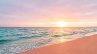 Serene tropical beach at sunrise with turquoise waves gently rolling onto soft pink sand, golden sunlight reflecting across calm ocean waters for travel and vacation concepts.