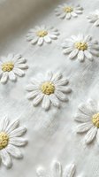 White daisy flowers embroidered on natural linen fabric with yellow centers creating delicate floral pattern for textile design and crafting projects.