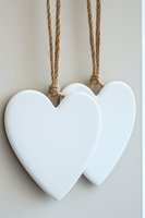 Two white wooden hearts hanging on natural rope against neutral background for romantic home decor and craft projects.