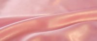 Soft pink silk fabric with elegant flowing waves and lustrous sheen creates luxurious textile background for fashion and beauty projects.