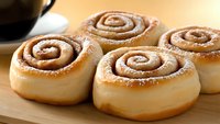 Freshly baked cinnamon rolls with spiral swirls of sweet filling, dusted with powdered sugar on wooden surface, close up view of soft fluffy pastries.