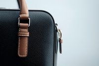 Close-up detail of black leather handbag with brown strap and metal buckle against light background, showcasing luxury accessories and fashion details.