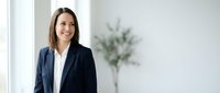 Professional businesswoman in navy suit smiling confidently in modern office environment with natural lighting and minimalist decor for corporate presentations.