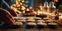 Freshly baked cookies cooling on wire rack with hand reaching for one, warm festive atmosphere with bokeh lights and candles in background.