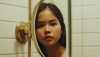 Young Asian woman with red lipstick gazing into bathroom mirror reflection, dramatic cinematic lighting creates moody atmosphere in intimate self-portrait scene.