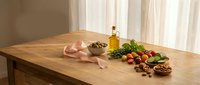 Fresh Mediterranean ingredients arranged on wooden kitchen table with olive oil, herbs, tomatoes and nuts for healthy cooking preparation.