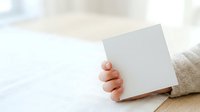 Young child with light skin tone holding blank white card or paper against neutral background, suitable for greeting cards, announcements, and promotional messaging.