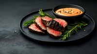 Medium rare beef steak slices on black plate with rosemary sprigs and creamy sauce with sesame seeds, served on dark background for restaurant menu.