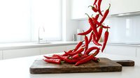 Fresh red chili peppers scattered on rustic wooden cutting board in modern white kitchen interior for culinary cooking and spicy food preparation.