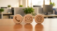 Wooden contact icons on office desk showing phone, email and at symbols for business communication and customer service concepts.