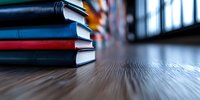 Stack of hardcover books on wooden table with blurred background, dramatic lighting and shallow depth of field creates moody academic atmosphere.