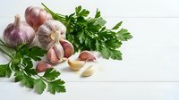 Fresh garlic bulbs and cloves with green parsley herbs on white wooden background for cooking and culinary preparations.