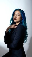 Professional businesswoman with vibrant blue hair in elegant black suit posing confidently against neutral background for corporate branding materials.