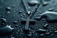 Silver cross pendant necklace on dark wet surface with water drops creating dramatic religious atmosphere. Macro photography with selective focus.