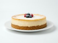 Cheesecake with graham cracker crust, creamy filling, and fresh berries on top, dusted with powdered sugar on white plate.