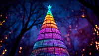Illuminated rainbow Christmas tree glowing against dark night sky with bokeh lights and tree silhouettes creating magical holiday atmosphere.