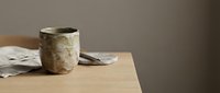 Rustic ceramic mug with natural glaze sitting on wooden table next to folded linen napkins, suitable for home decor and lifestyle photography.