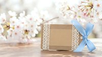 Handmade gift box with blue ribbon and lace decoration on wooden table with spring cherry blossoms in soft focus background for special occasions.