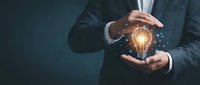 Businessman in dark suit holding glowing lightbulb with sparkling particles, representing innovation, creativity, and business ideas for corporate and entrepreneurial concepts.