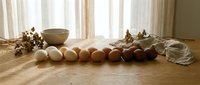 Fresh brown eggs arranged on rustic wooden table with natural cotton branches and ceramic bowl in warm sunlit kitchen setting for cooking.