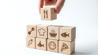 Hand placing wooden cube with fork knife symbol on stack of food-themed blocks representing culinary concepts and restaurant business planning.