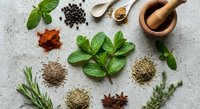 Fresh herbs and spices arranged on stone surface with wooden mortar and pestle for natural cooking and seasoning in culinary kitchen preparation.