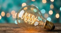 Vintage Edison bulb with glowing filament on wooden surface against turquoise bokeh lights background creating warm atmospheric lighting for creative projects.