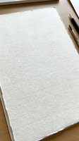 Blank watercolor paper sheet with textured surface on wooden desk with pencils ready for artistic creation and drawing projects.