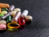Colorful assortment of medical pills, tablets, and supplements scattered on dark slate background with selective focus and copy space for healthcare concept.