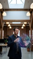 Professional businessman presenting holographic data visualization in modern loft office with exposed brick walls and pendant lighting for business technology concepts.