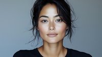 Young Asian woman with natural makeup and black messy bun hairstyle wearing dark top against gray background, looking directly at camera with confident expression.