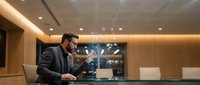 Professional businessman using laptop in modern office conference room with city lights background for corporate presentations and meetings.