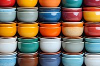 Colorful ceramic bowls stacked in rows showing vibrant glazed finishes from red to blue, orange to white, creating modern kitchen decor pattern for dining and serving.