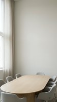 Minimalist meeting room with light wood oval table, gray upholstered chairs, and floor-to-ceiling windows with neutral curtains for corporate office design.