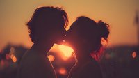 Romantic couple silhouettes kissing at golden sunset creating heart shape with warm orange glow. Perfect for love, romance and relationship concepts.