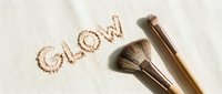 Makeup brushes with glow text written in shimmering powder on white surface, cosmetics and beauty product styling for makeup artist tutorials and skincare branding.