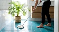 Woman mopping turquoise tile floor in modern kitchen with palm plant, home cleaning and housework routine for maintaining hygiene and cleanliness.