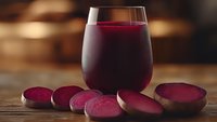 Fresh beetroot juice in glass with sliced raw beets on wooden table. Healthy vegetable drink for detox and wellness lifestyle.