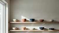 Minimalist ceramic bowls displayed on floating wooden shelves in modern kitchen interior with natural lighting and neutral beige wall background.