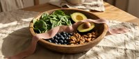 Healthy breakfast bowl with fresh arugula, sliced avocado, blueberries and nuts in wooden dish on rustic table for nutritious morning meal preparation.