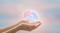 Hands holding glowing digital brain with pink and blue light particles against soft sky background, representing artificial intelligence, innovation, and technology concepts.