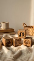 Wooden toy blocks with engraved symbols including house, scales, tree and dancing figures on cozy knitted blanket with warm natural lighting and home decor.