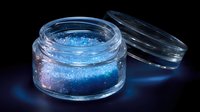 Luminescent blue glitter powder in clear glass jar with open lid against dark background, creating magical glow effect for cosmetic and artistic projects.