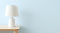 Minimalist white ceramic table lamp with linen shade on wooden nightstand against pale blue wall, contemporary home decor.